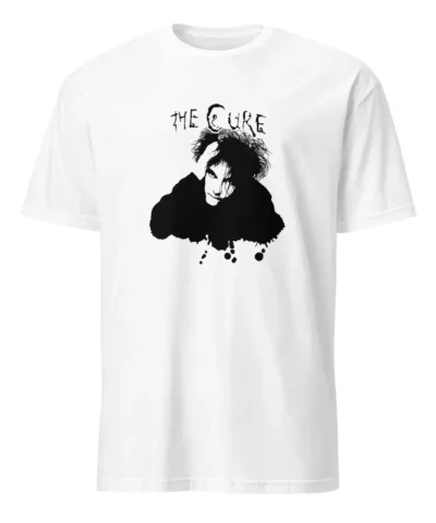 Uma mulher jovem e sorridente, com cabelo encaracolado, veste uma t-shirt branca de mangas curtas. A t-shirt tem uma estampa preta de Robert Smith, vocalista da banda The Cure. A mulher está a ajustar o cabelo com uma das mãos, enquanto a outra mão está na anca. O fundo desfocado mostra plantas de interior e móveis brancos, sugerindo um ambiente doméstico.