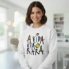 Uma mulher jovem e sorridente com cabelo castanho curto, a usar uma sweatshirt branca com a frase colorida 'A VIDA É TÃO RARA' estampada em estilo artístico. O fundo é um interior moderno e luminoso.
