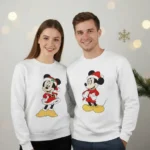 Casal a usar sweatshirts de Natal unissexo brancas com estampa festiva de personagem clássico com gorro de Pai Natal.