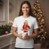 Ursinho vestido de Papai Noel segurando um presente e um sino, ilustrado em estampa sobre T-shirt branca.