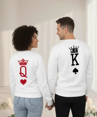 Fotografia de costas de um casal de mãos dadas, vestindo sweatshirts brancas unissexo. A peça da esquerda apresenta uma coroa vermelha sobre a letra Q e um coração; a da direita exibe uma coroa preta sobre a letra K e um símbolo de espadas.