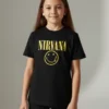 -shirt preta infantil com o logótipo amarelo do Nirvana e a "Smiley Face" no peito, em fundo branco.