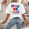 Vista de costas da t-shirt marfim com grafismo grande e colorido "Now or Never - Love Today" e corações estilizados.