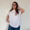 Modelo feminina veste t-shirt oversized marfim com pequena estampa colorida "Now or Never" no peito e calças de ganga azuis.