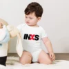 Body de bebé branco de manga curta com o logótipo oficial da banda INXS estampado no peito em preto e vermelho.