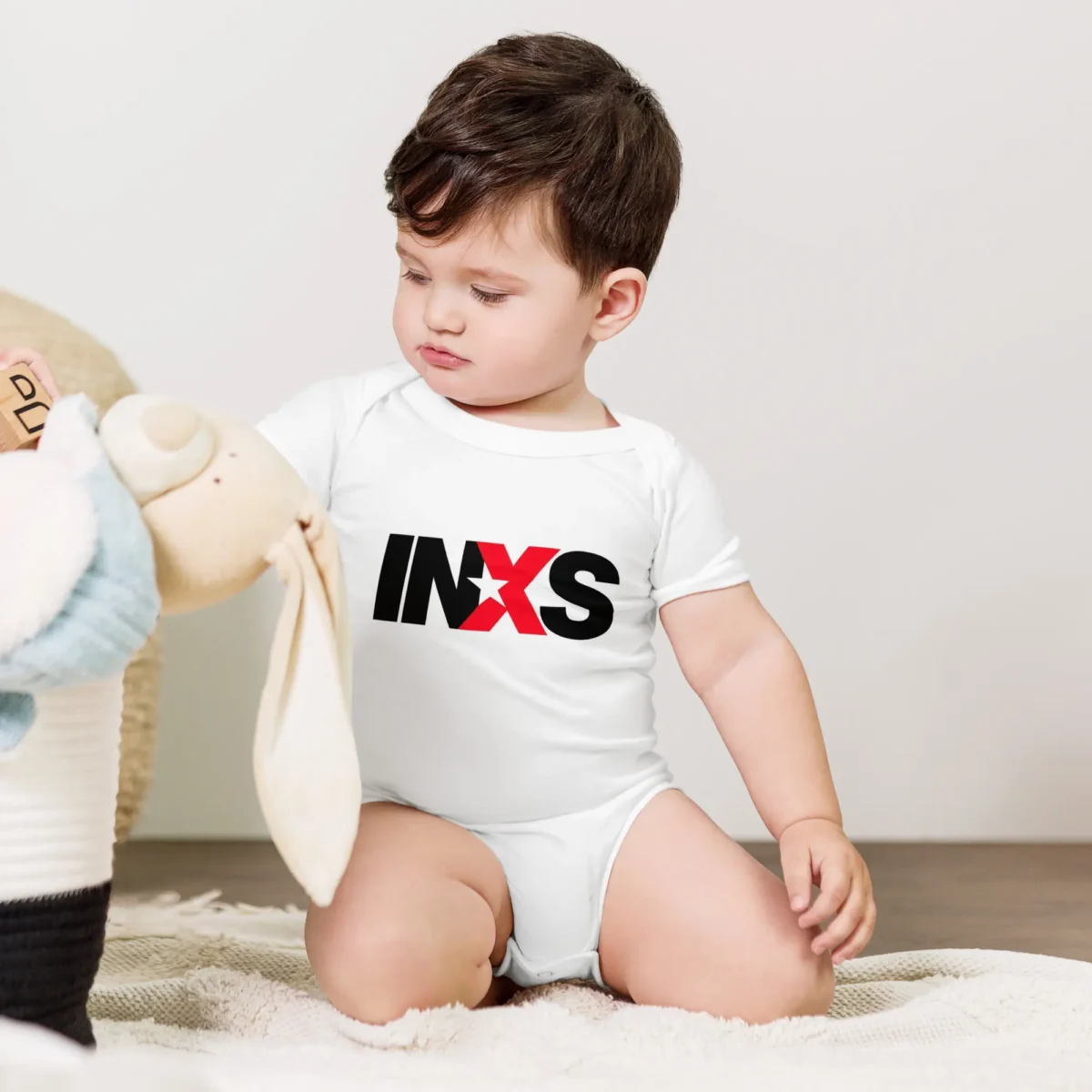 Body de bebé branco de manga curta com o logótipo oficial da banda INXS estampado no peito em preto e vermelho.